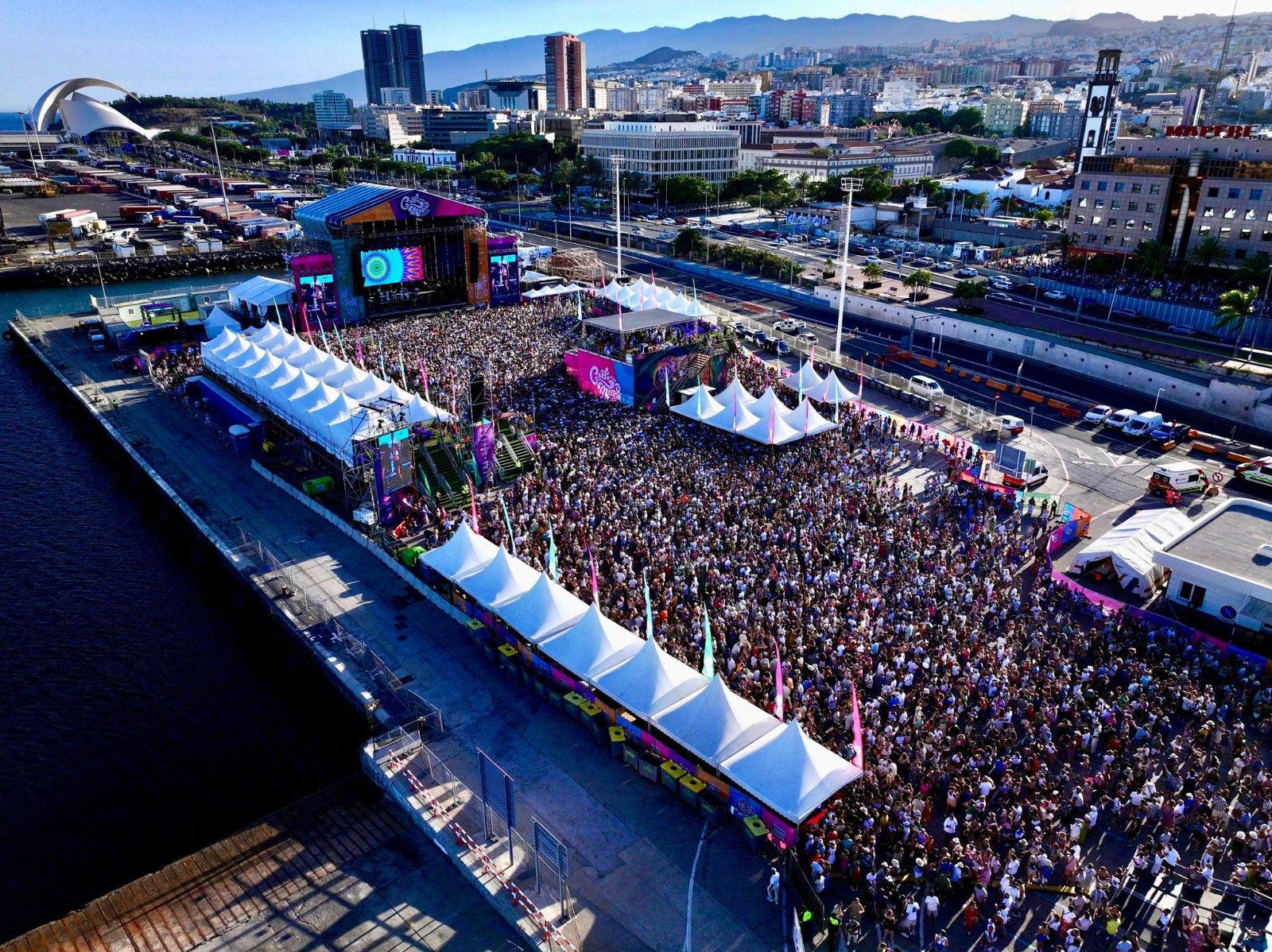 Vista aérea de un festival junto al puerto de Santa Cruz de Tenerife, con miles de asistentes frente al escenario